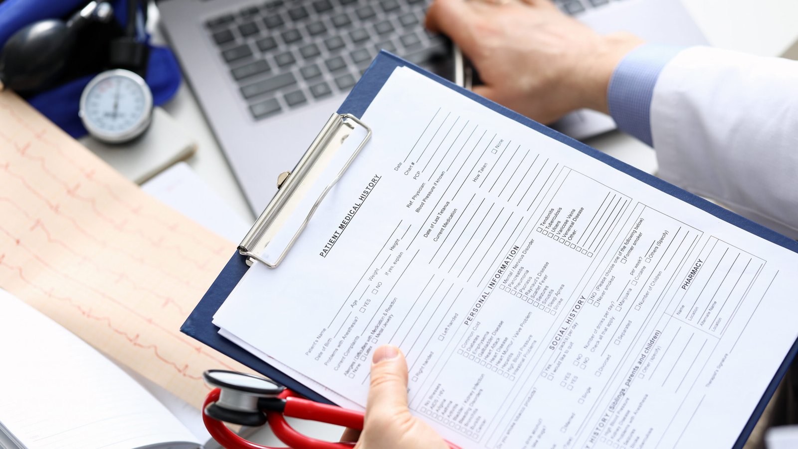 Doctor reviewing a patient medical records form with a laptop in the background, representing the importance of medical documentation in maximizing injury settlements in Pasadena and Alhambra, CA.