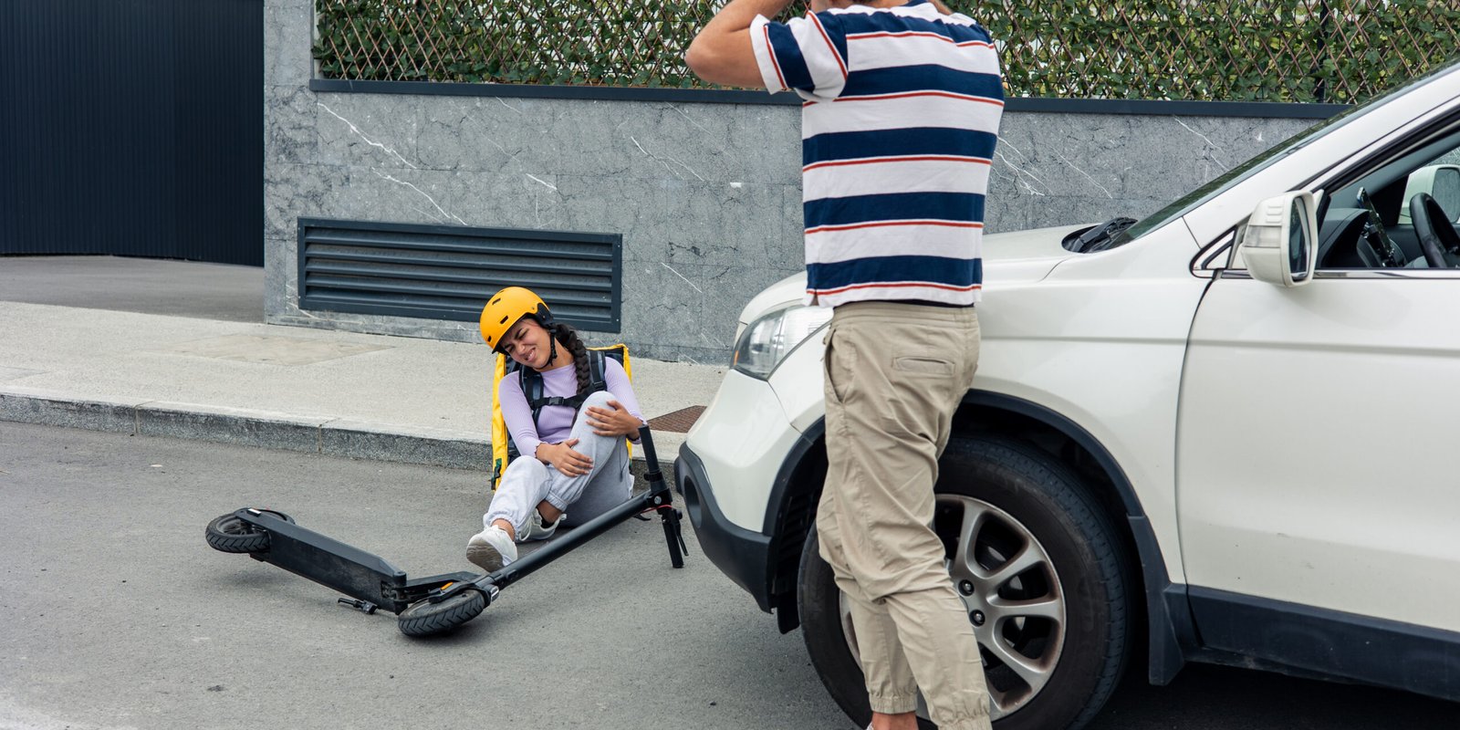 E-Scooter Accident Victim with Legal Rights Advice A young woman with a helmet sitting on the ground after e-scooter accidents, while a person calls for help. The scene is in an urban area.