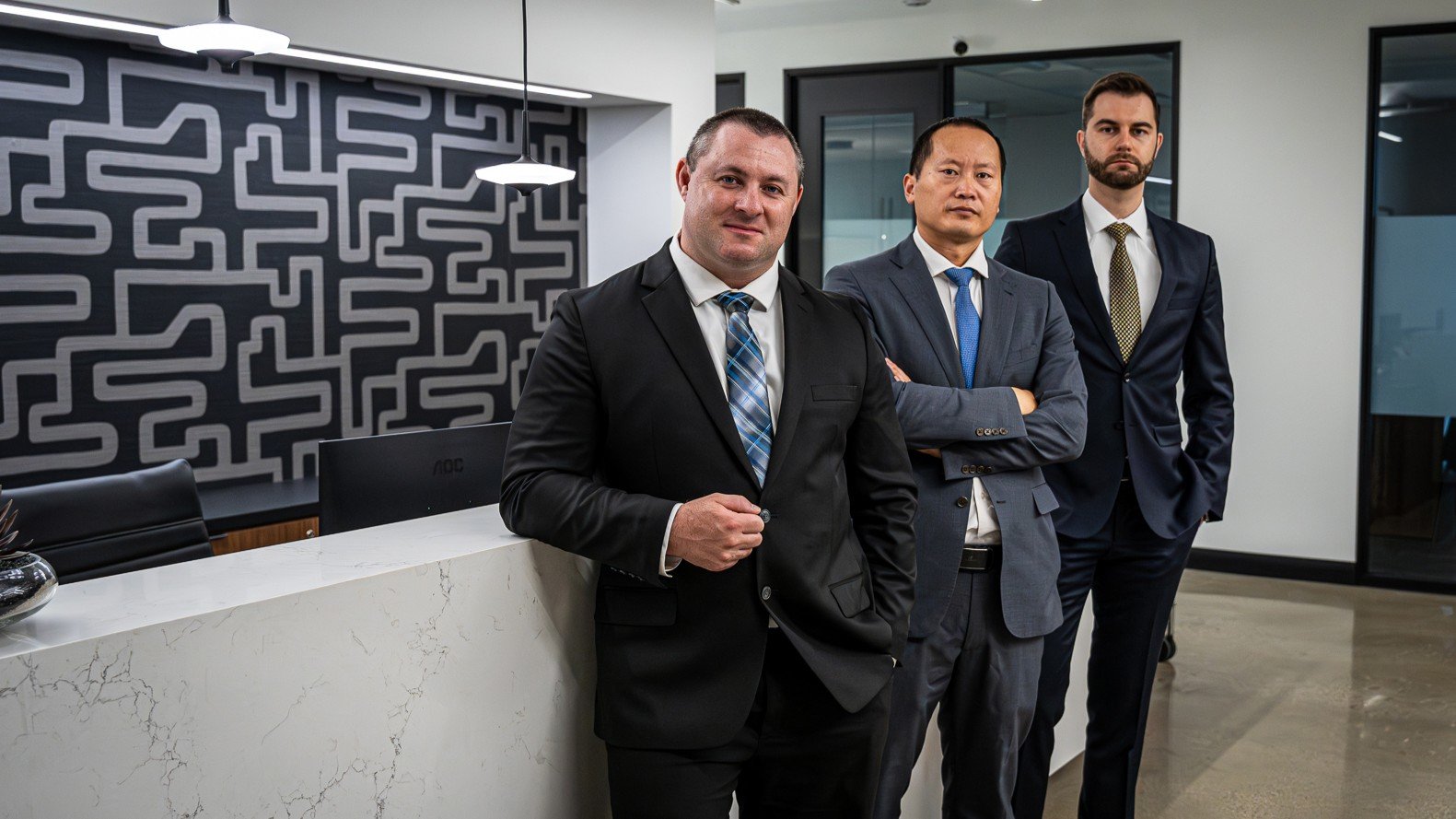 A group of three attorneys dressed in business suits stand confidently in a modern law office. The background features a contemporary design, indicating a professional and trusted legal team.