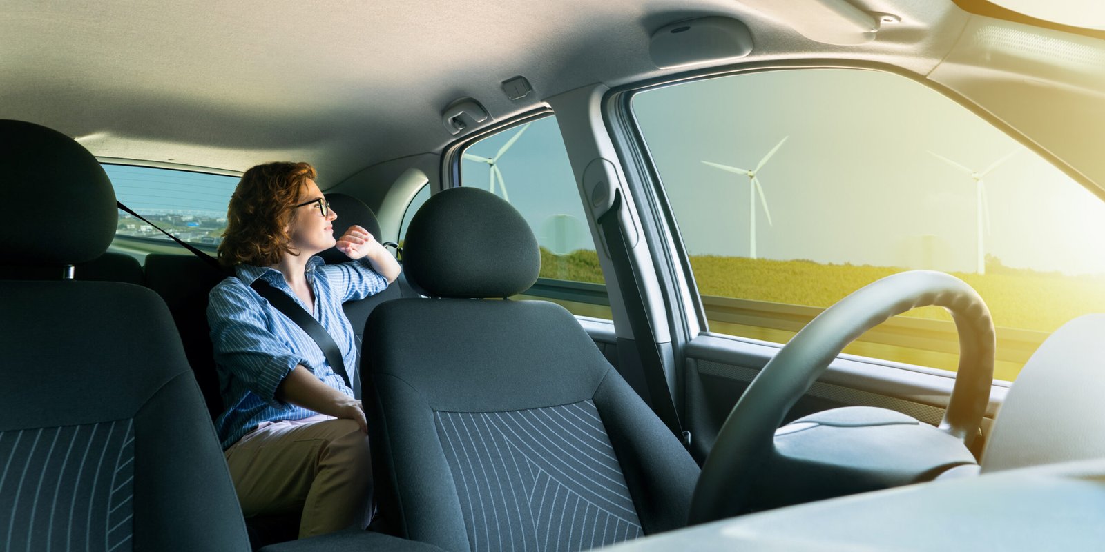 A woman looks out the window of a car, gazing at wind turbines as the car drives along a scenic road, representing the future of autonomous travel. A woman looks out the window of a car, gazing at wind turbines as the car drives along a scenic road, representing the future of autonomous travel.