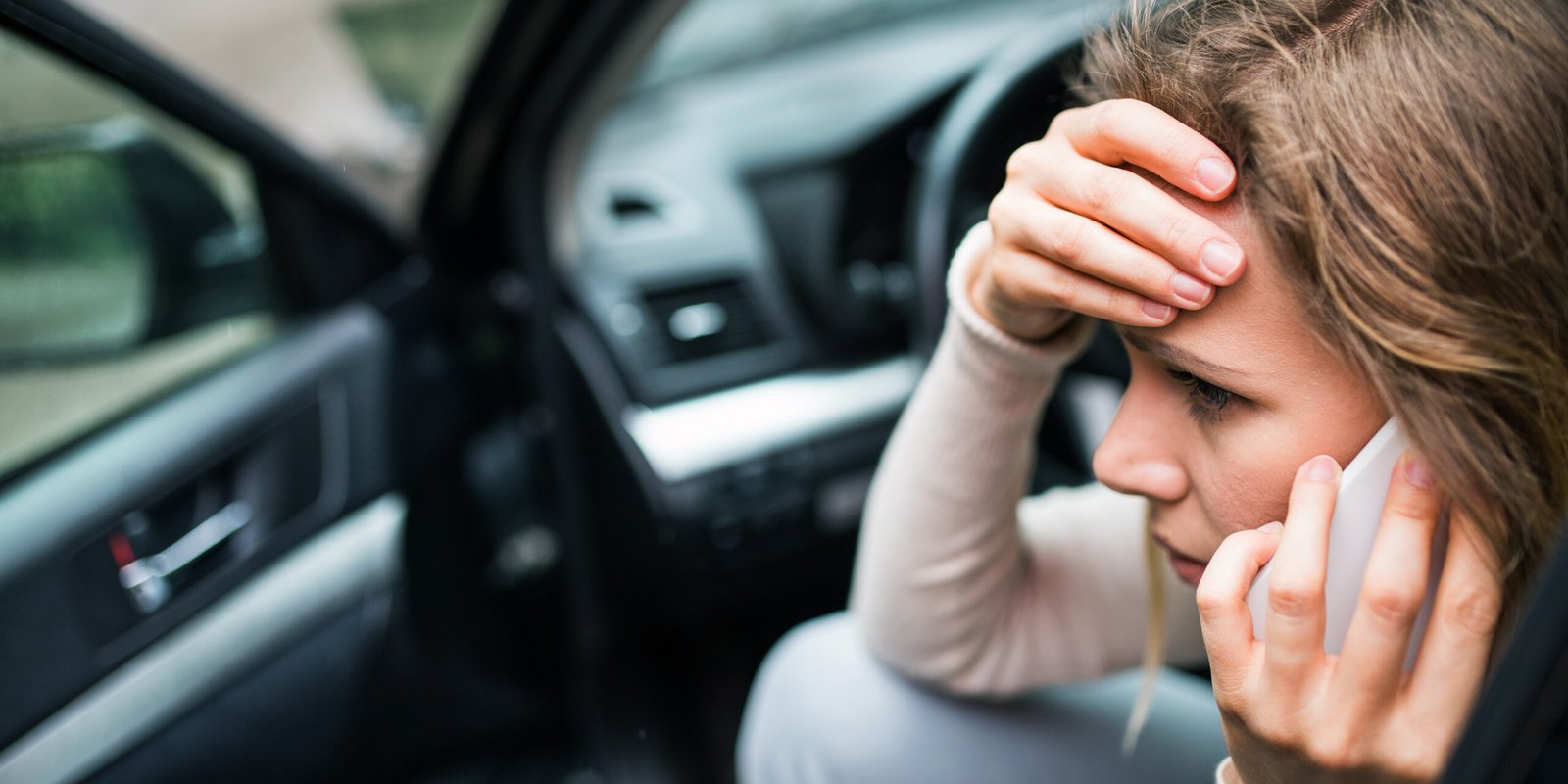 Woman Stressed After Car Accident Speaking on the Phone A stressed woman in her car holds her head while speaking on the phone after a car accident, showing signs of distress.