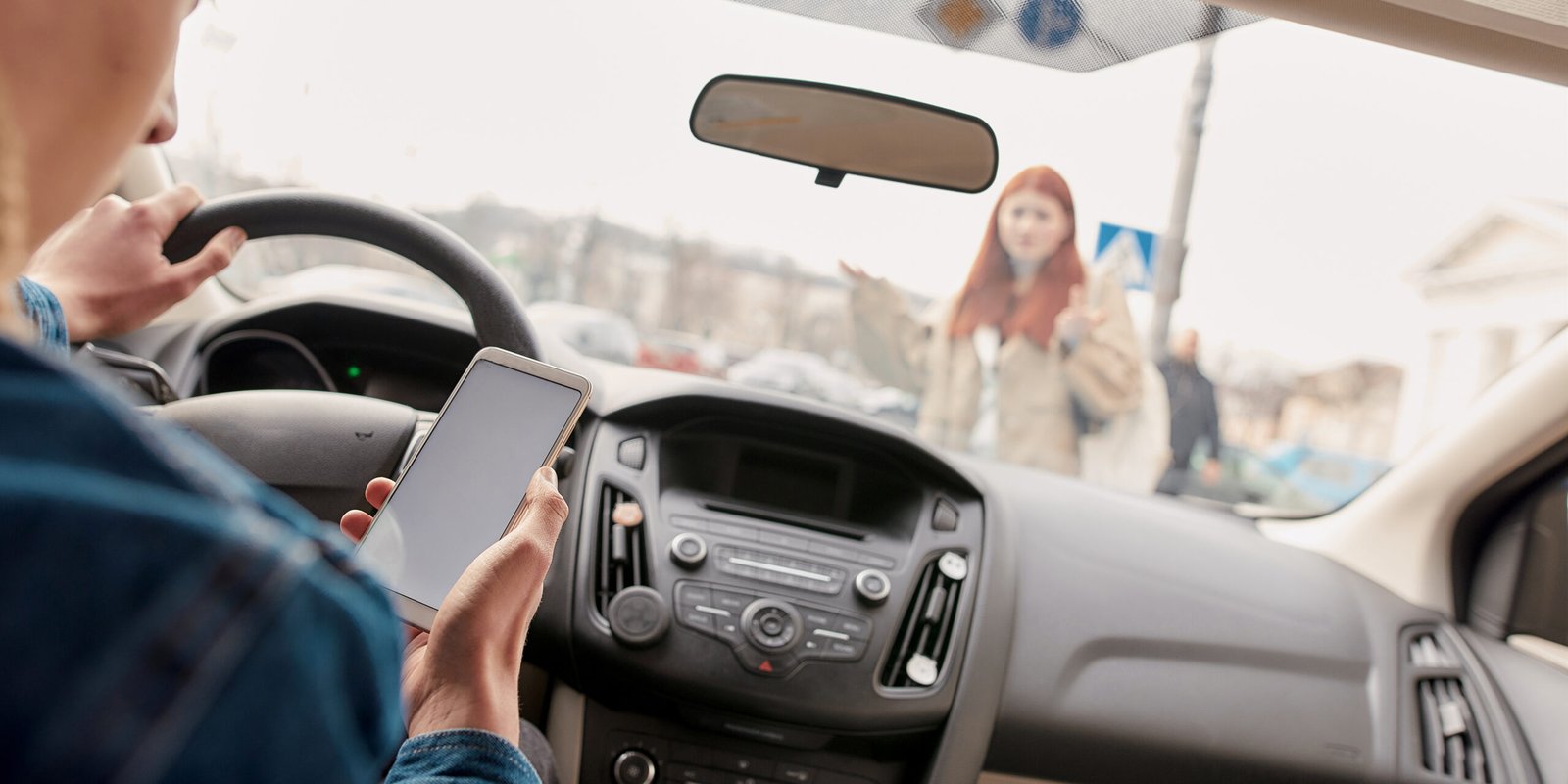 A driver inside a car distracted by a smartphone with a pedestrian standing ahead, arms raised in confusion, capturing the dangers that can lead to a pedestrian accident.