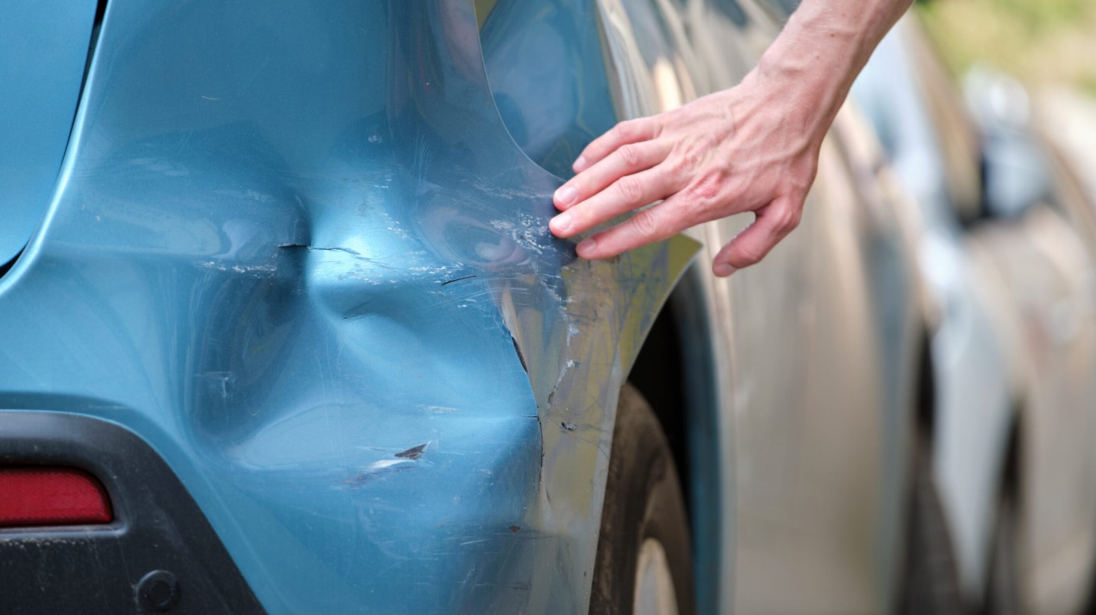 Person examining dents and scratches on a blue car’s rear fender, showing how to inspect and record evidence after a hit-and-run accident in Los Angeles or Orange County.