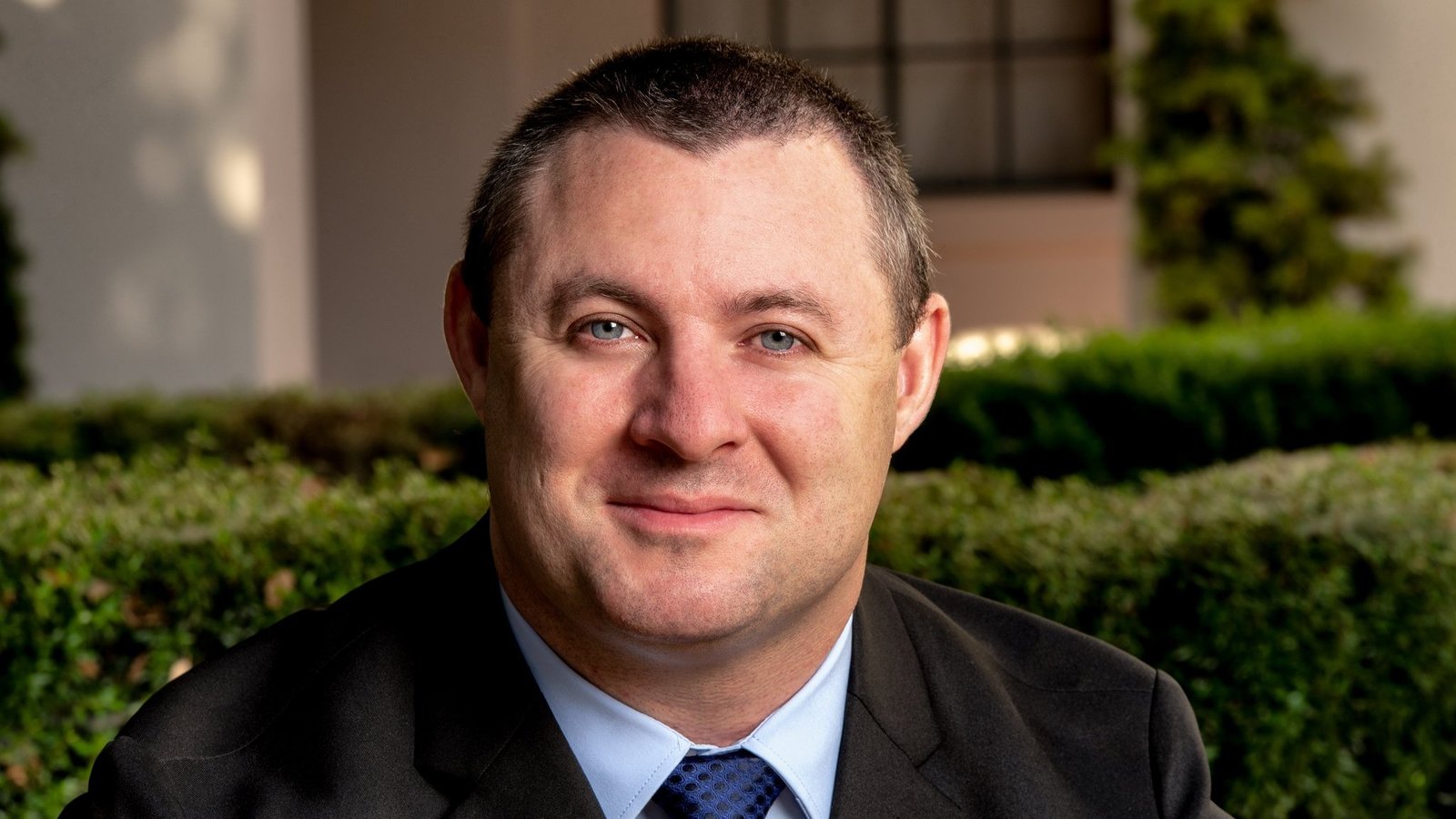 Professional portrait of James Doyle, a personal injury attorney, smiling outdoors in a suit, representing dedication and trustworthiness for clients needing strong legal support after an accident.