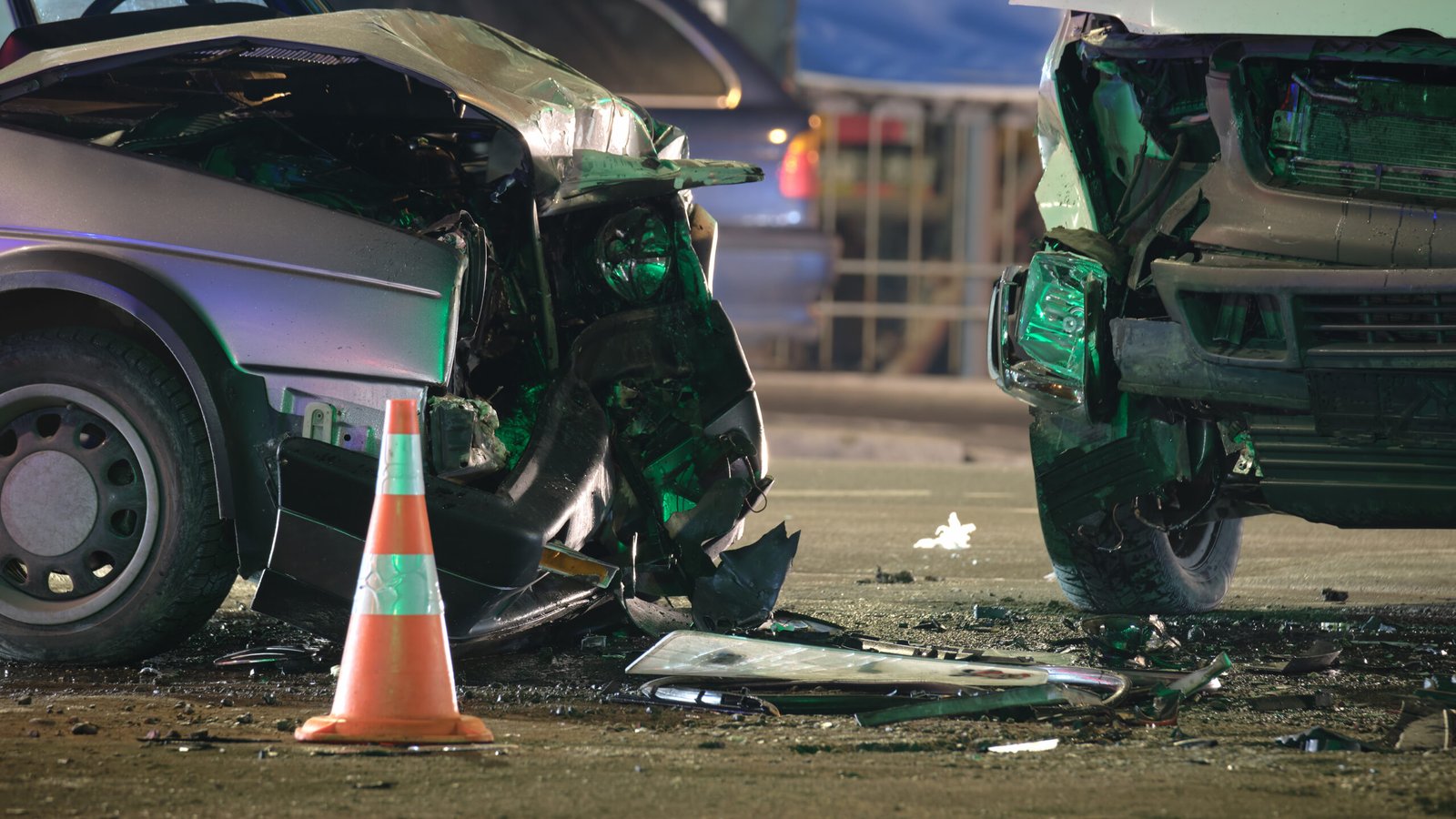 Two heavily damaged cars at the scene of a nighttime car accident in California, with debris and a traffic cone visible on the road.