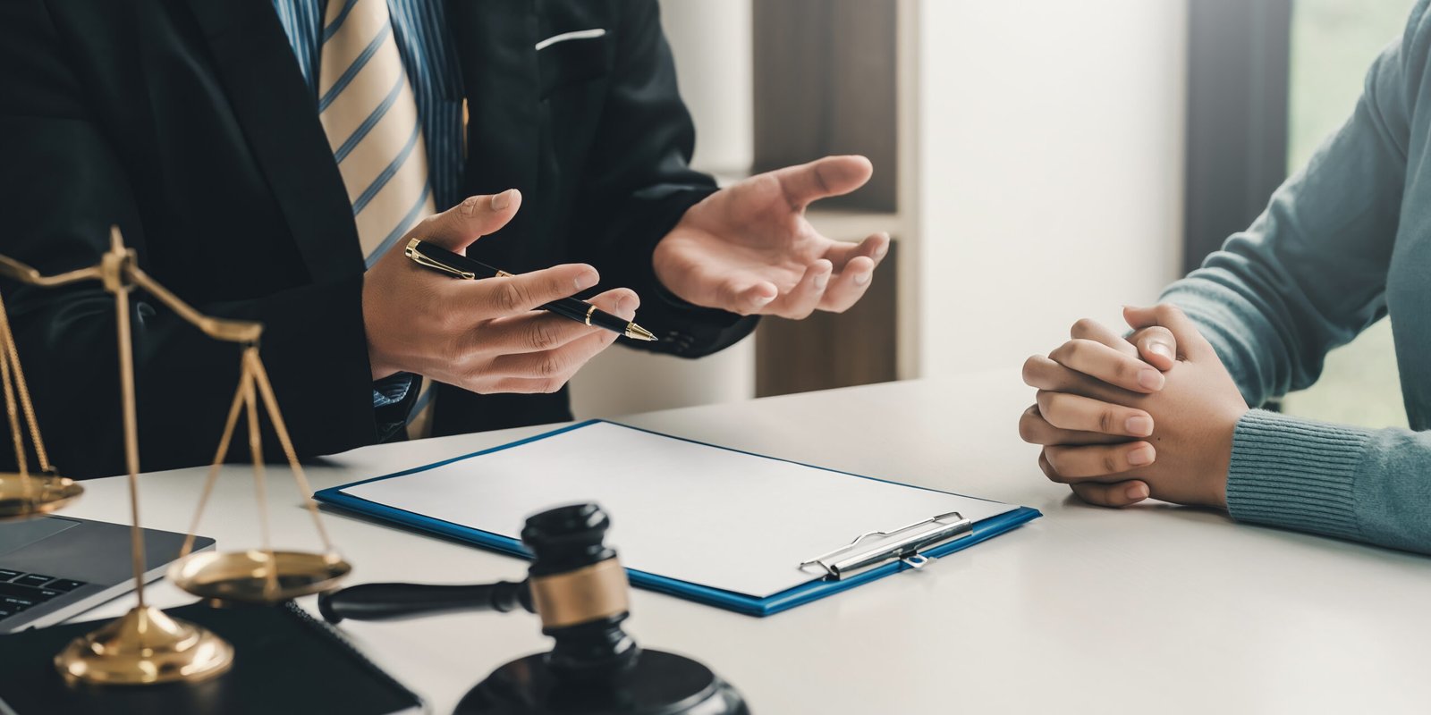 Personal injury attorney discussing a case with a client about being injured at a gym, with legal documents, gavel, and scales of justice on the desk.