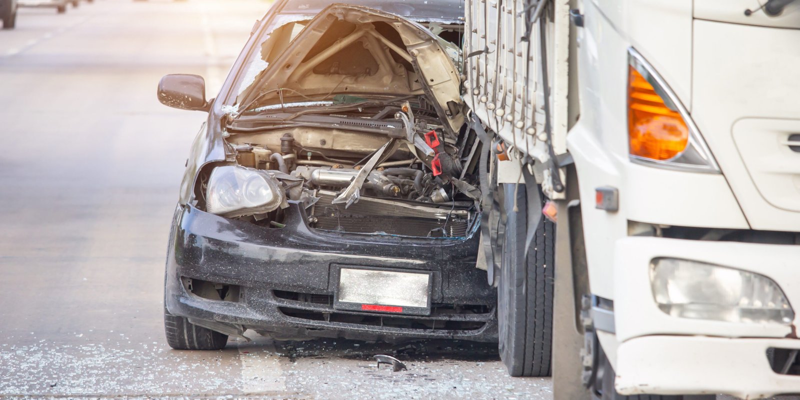 A severely damaged black car with its front end crushed after a collision with a large white truck on a Southern California road. The scene shows extensive vehicle damage, perfect for an article about truck accidents.