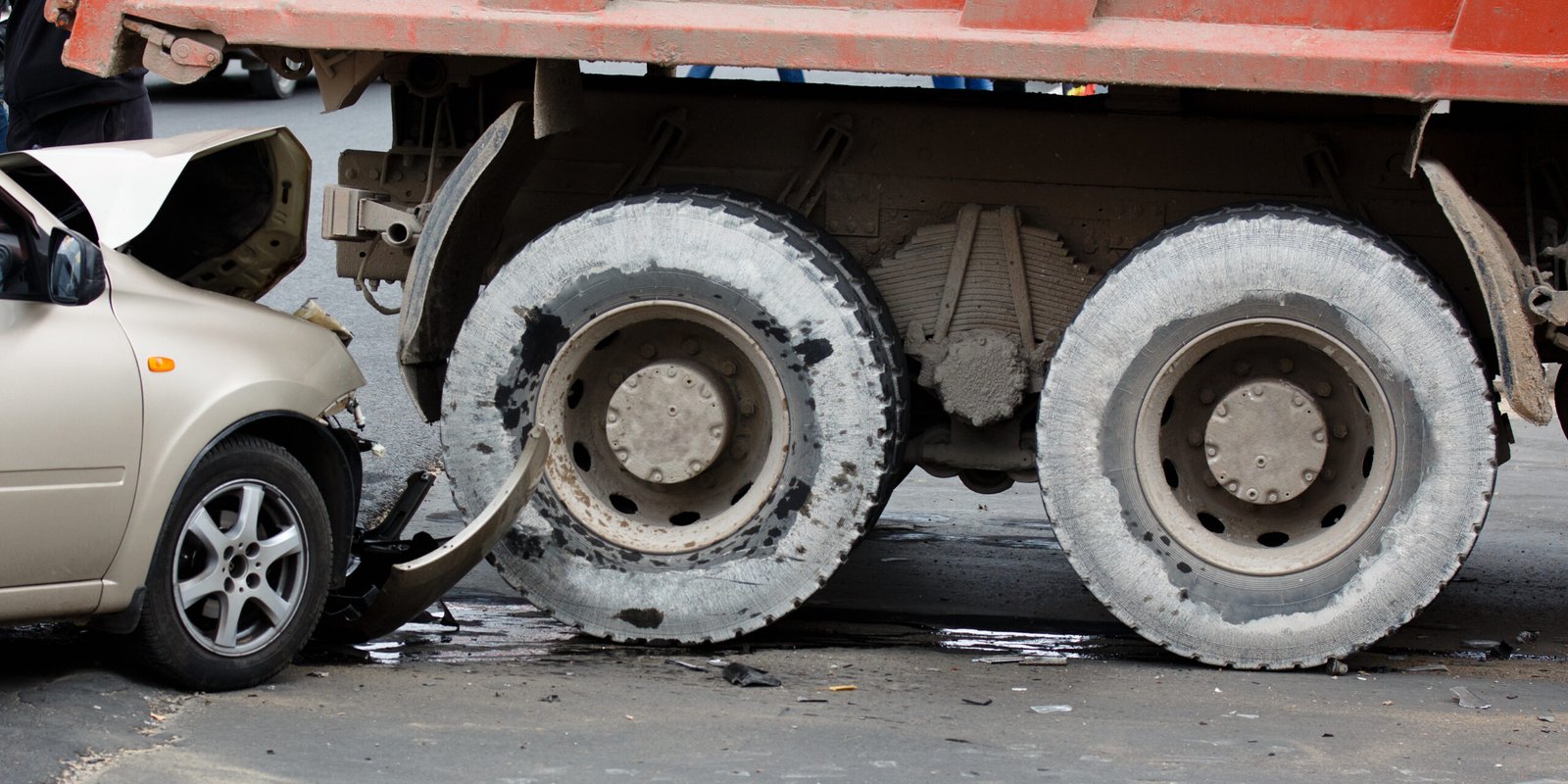 A beige car lodged underneath the rear of a large commercial truck with visible wheel damage and body dents, illustrating the dangers and severity of a truck accident in Southern California.
